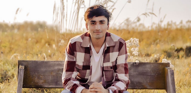 Tomas smiles on a bench with a field in the background.